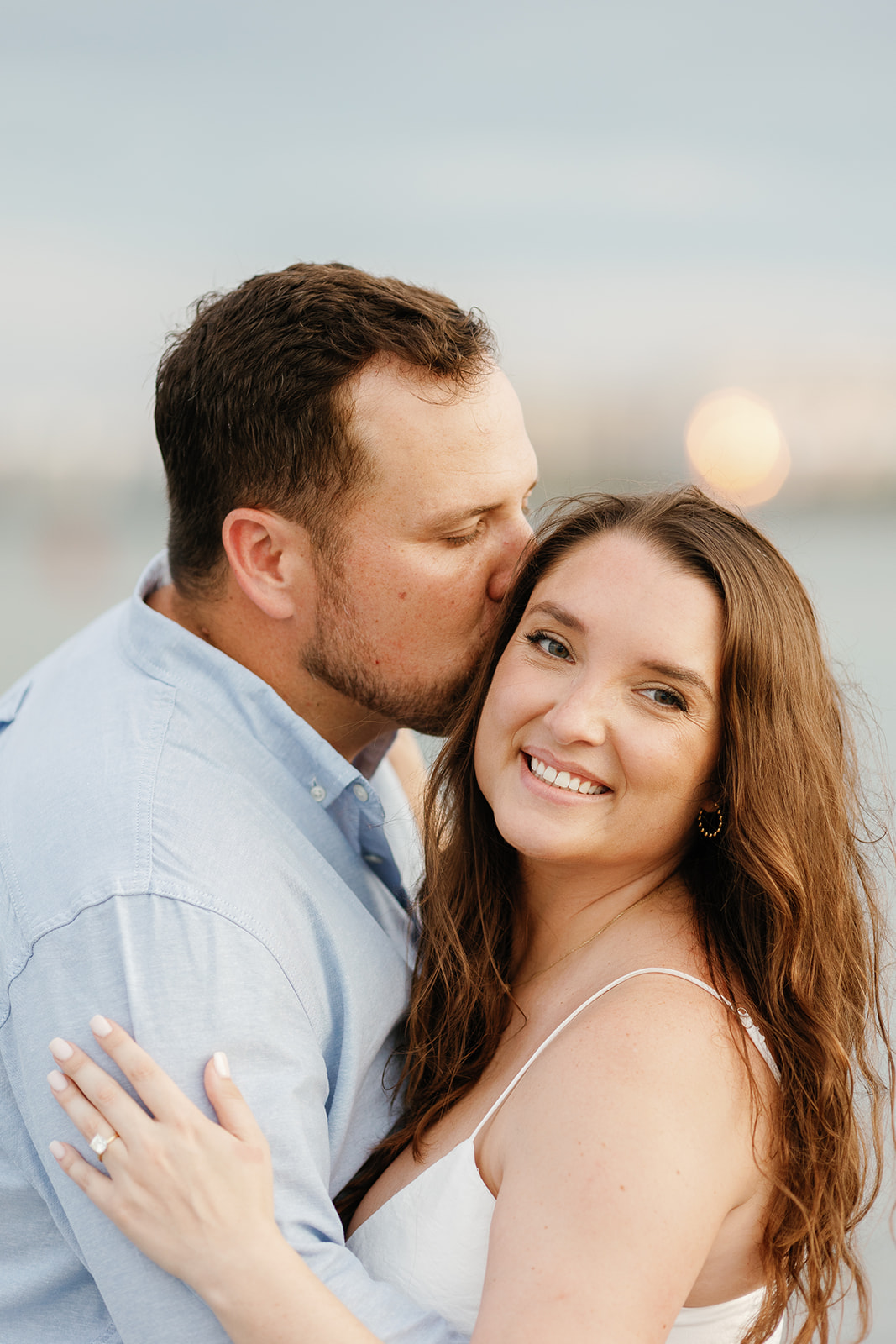 Engagement photo on the beach where the man gently gives his fiancé a kiss on the forehead.