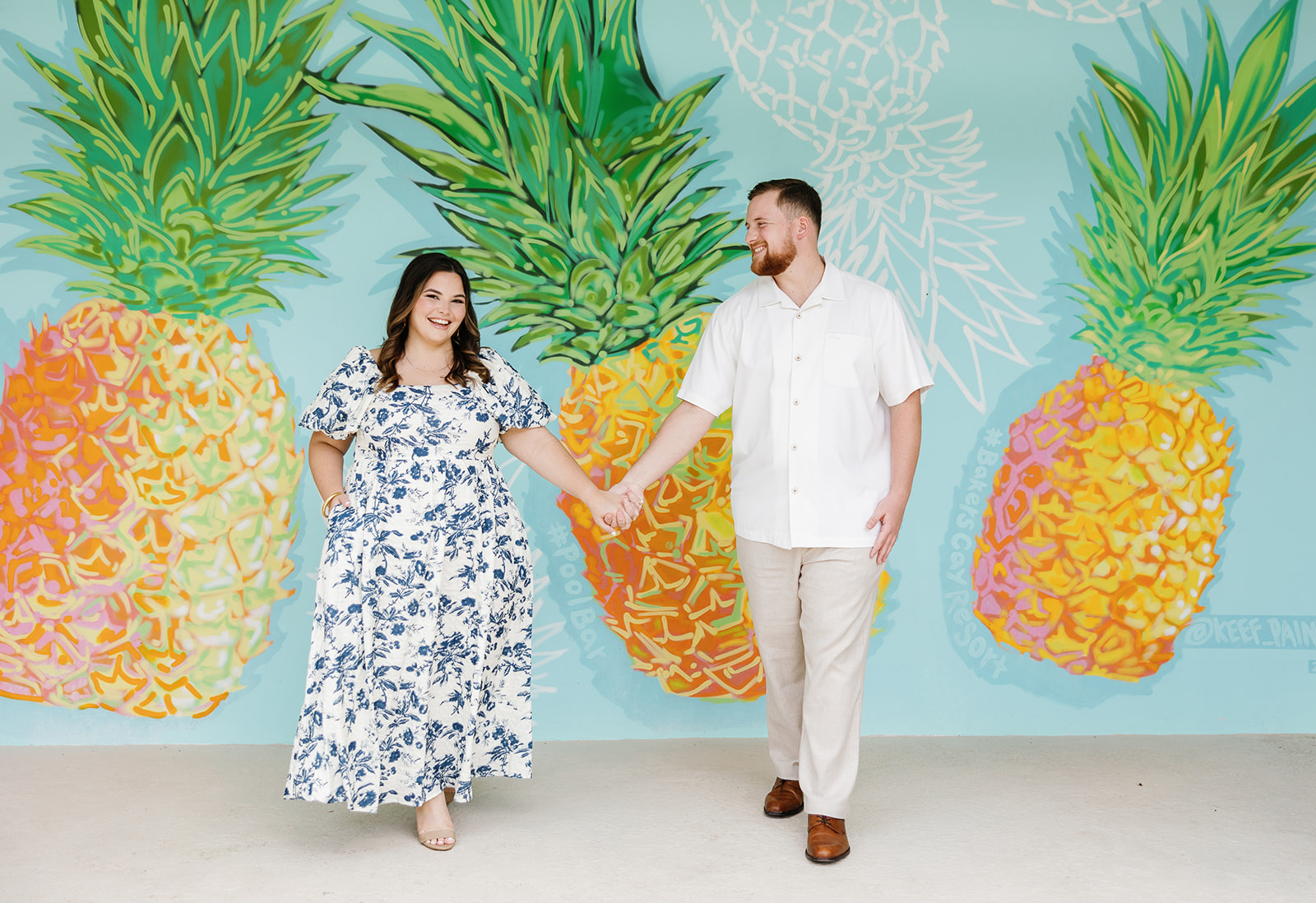 Claire and Reece share a joyful moment in front of the vibrant pineapple mural at Bakers Cay Resort, captured by a Key Largo wedding photographer.