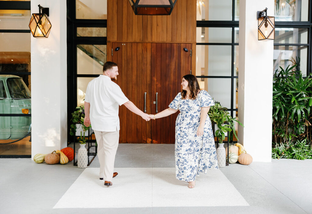 Claire and Reece walk hand in hand in front of the stylish entrance at Bakers Cay Resort, a stunning location for engagement photography.