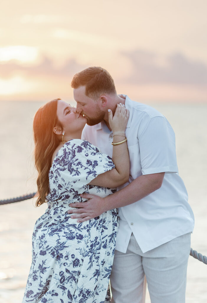 Claire and Reece share a romantic kiss on the dock at sunset, their love glowing in the golden light—captured by a destination wedding photographer.