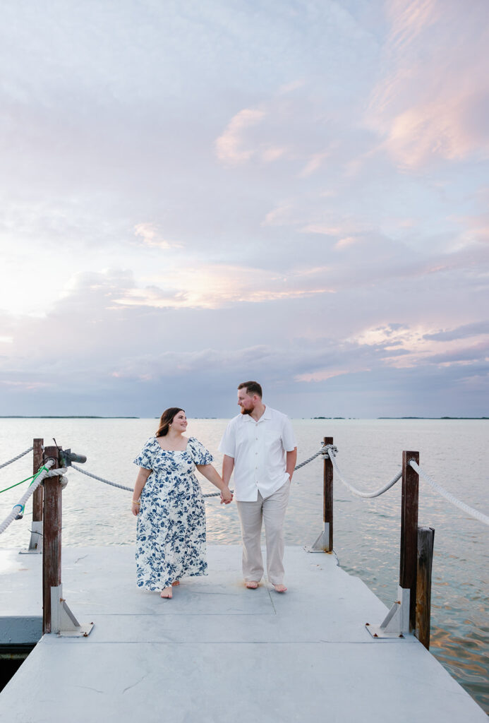 Hand in hand, Claire and Reece walk barefoot along the dock at Baker’s Cay Resort, with the Florida sunset reflecting on the ocean behind them. A dreamy moment from their engagement session.