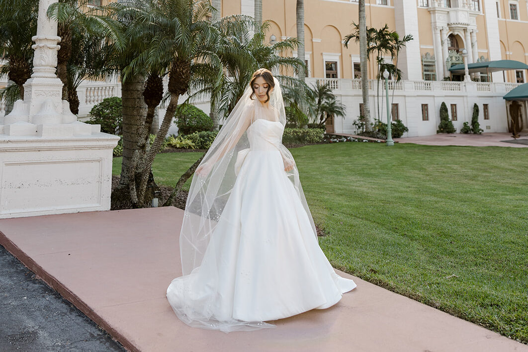 Bride in a white gown posing at Biltmore Hotel Coral Gables with the sun peeking through palm trees.