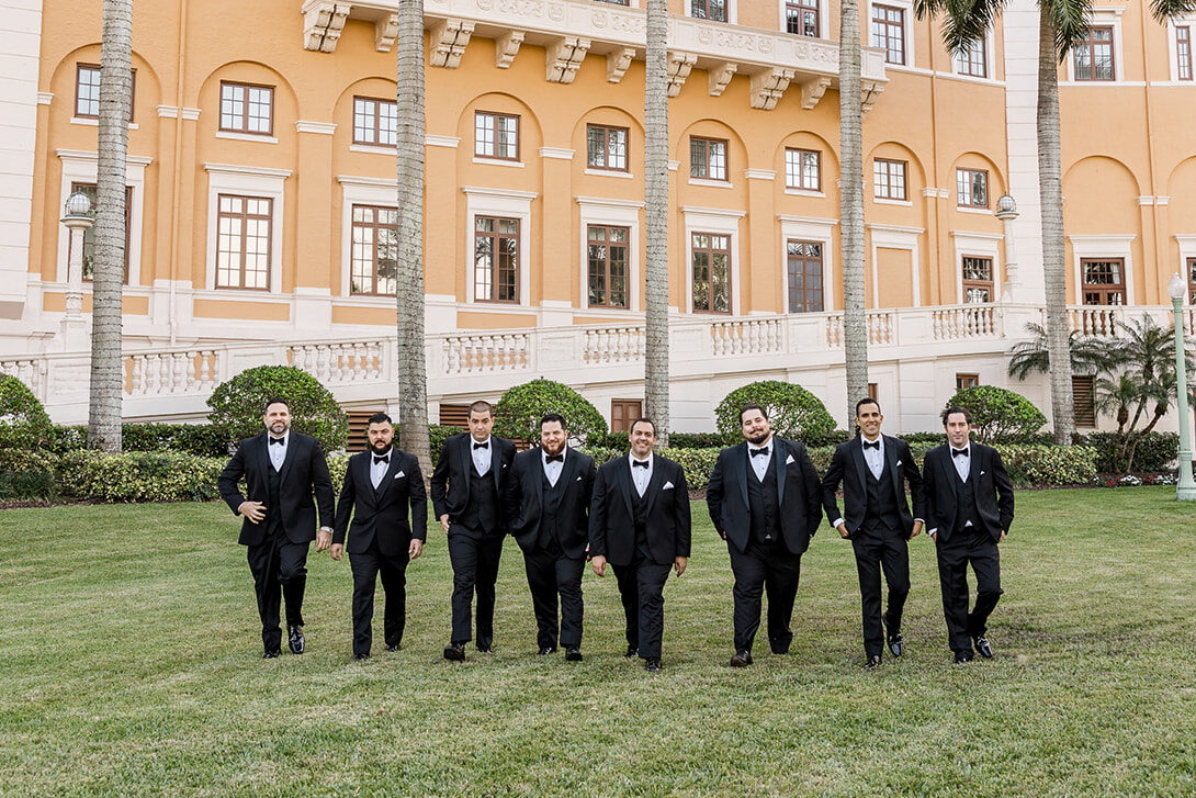 Groom and groomsmen in black tuxedos walking on the lawn at Biltmore Hotel Coral Gables.