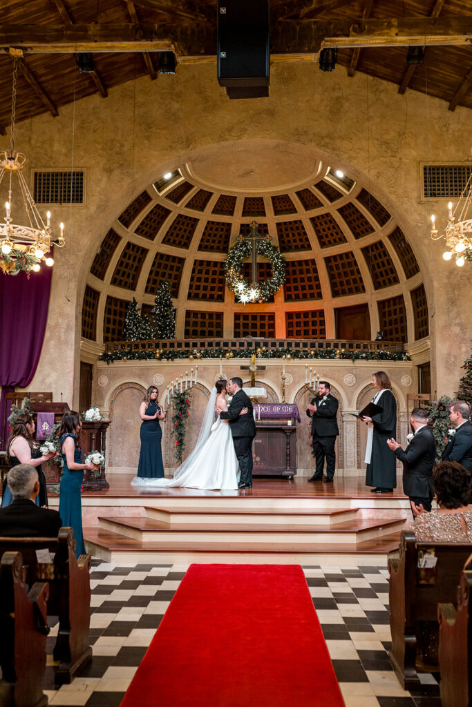 Bride and groom sharing their first kiss inside a historic church with Christmas decor.