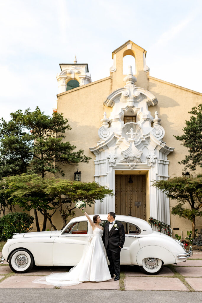 Bride and groom celebrate in front of a vintage white car at Biltmore Hotel Coral Gables.