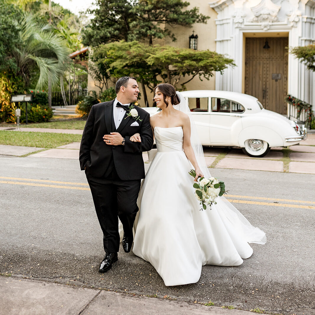 Newlyweds walk hand-in-hand in front of the Biltmore Hotel Coral Gables.