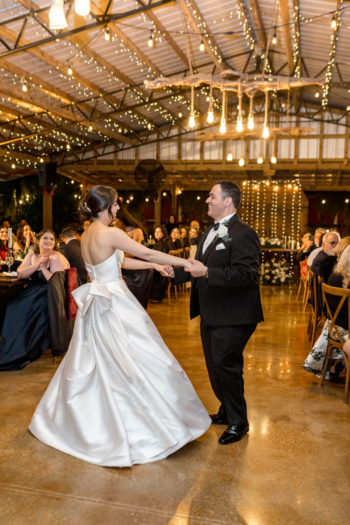 The couple’s first dance at their reception, with guests seated around them in a warm, intimate setting.