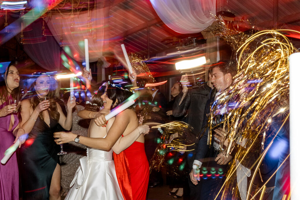 Wedding guests dancing and celebrating under colorful party lights.