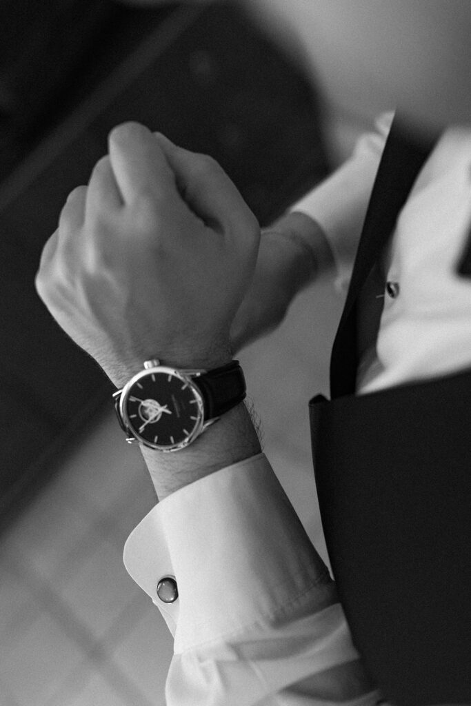 A black-and-white close-up of the groom adjusting his watch, emphasizing timeless elegance.