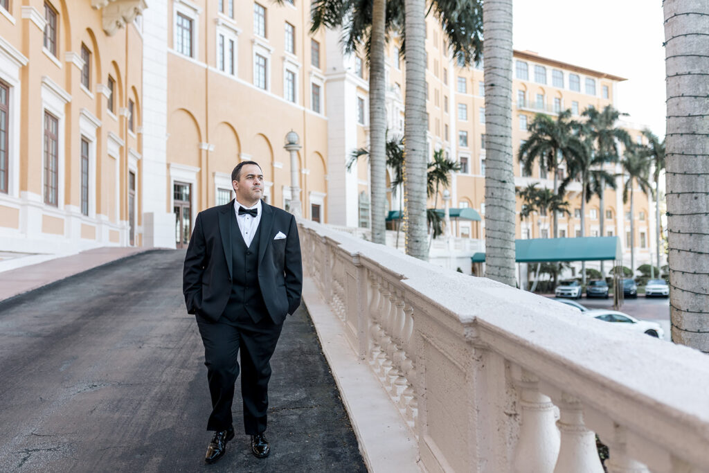 Groom walking confidently outside the grand Biltmore Hotel, dressed in a black tuxedo.