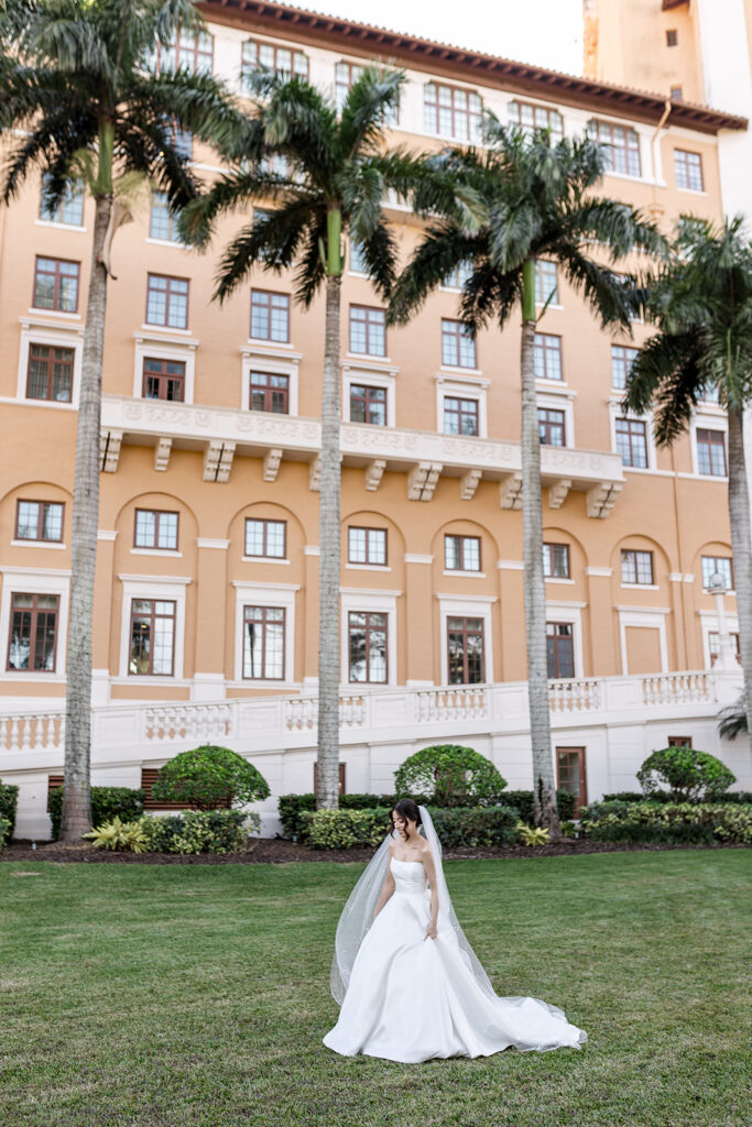 Bride in a white wedding gown walks across the green lawn at the Biltmore Hotel.