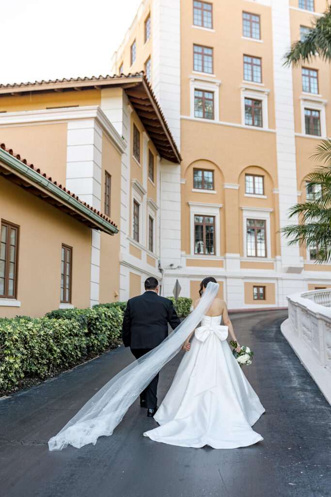 Bride and groom walking hand-in-hand outside the Biltmore Hotel, her veil flowing.