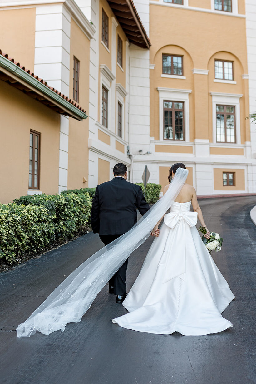 Bride and groom walking hand-in-hand outside the Biltmore Hotel, her veil flowing.