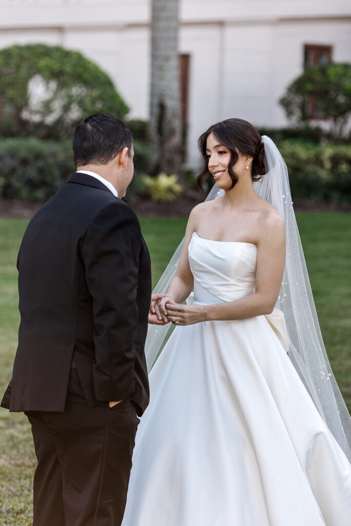 Bride and groom smile at each other while holding hands during their first look.