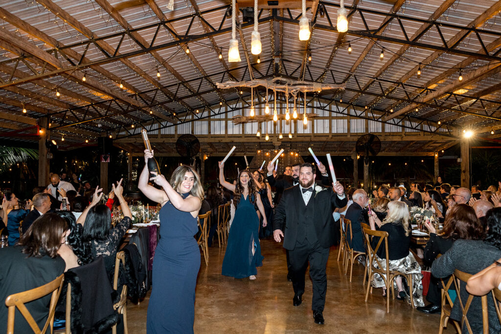 Grand entrance of wedding reception with guests cheering under warm string lights.