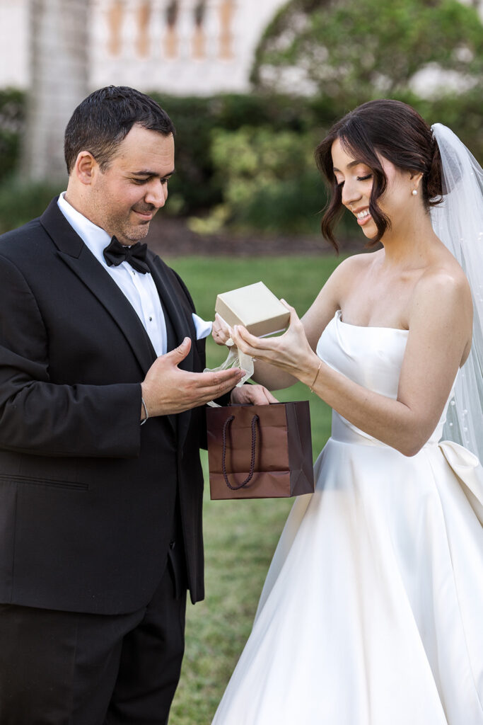 Groom hands a beautifully wrapped gift to his bride, who smiles with excitement.