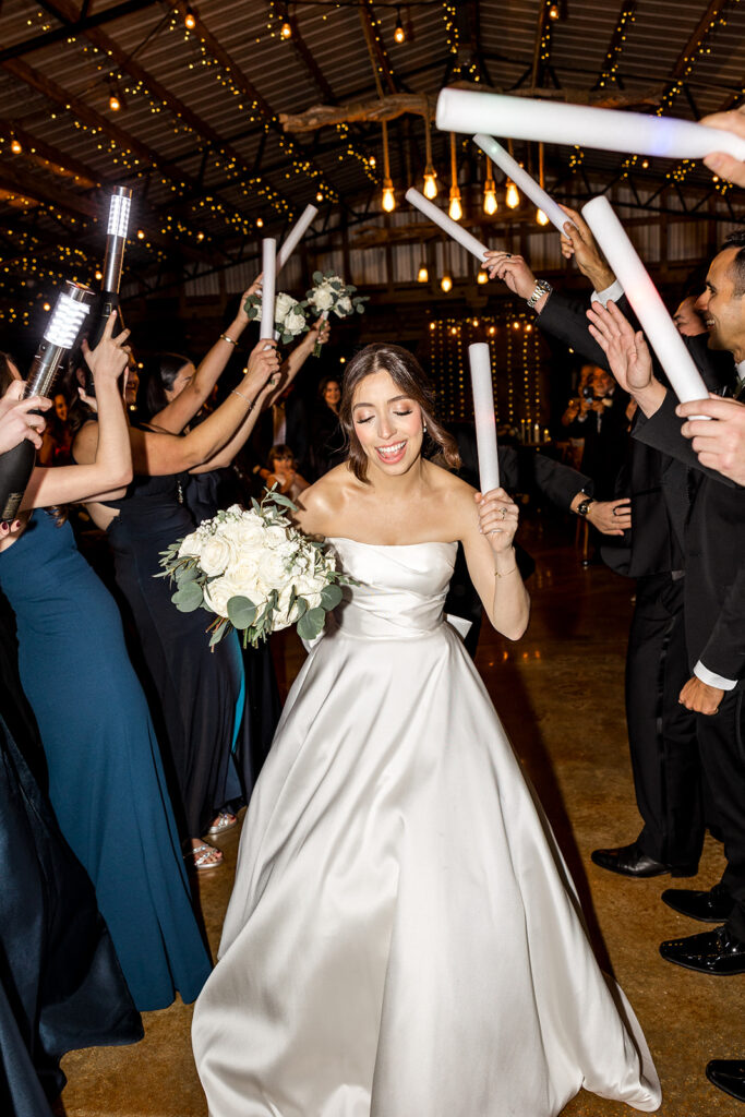 Bride dancing with joy during the wedding reception, holding a bouquet and glow stick.