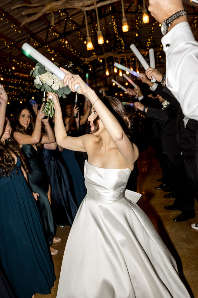 Bride dancing with arms raised, celebrating with wedding guests at reception.