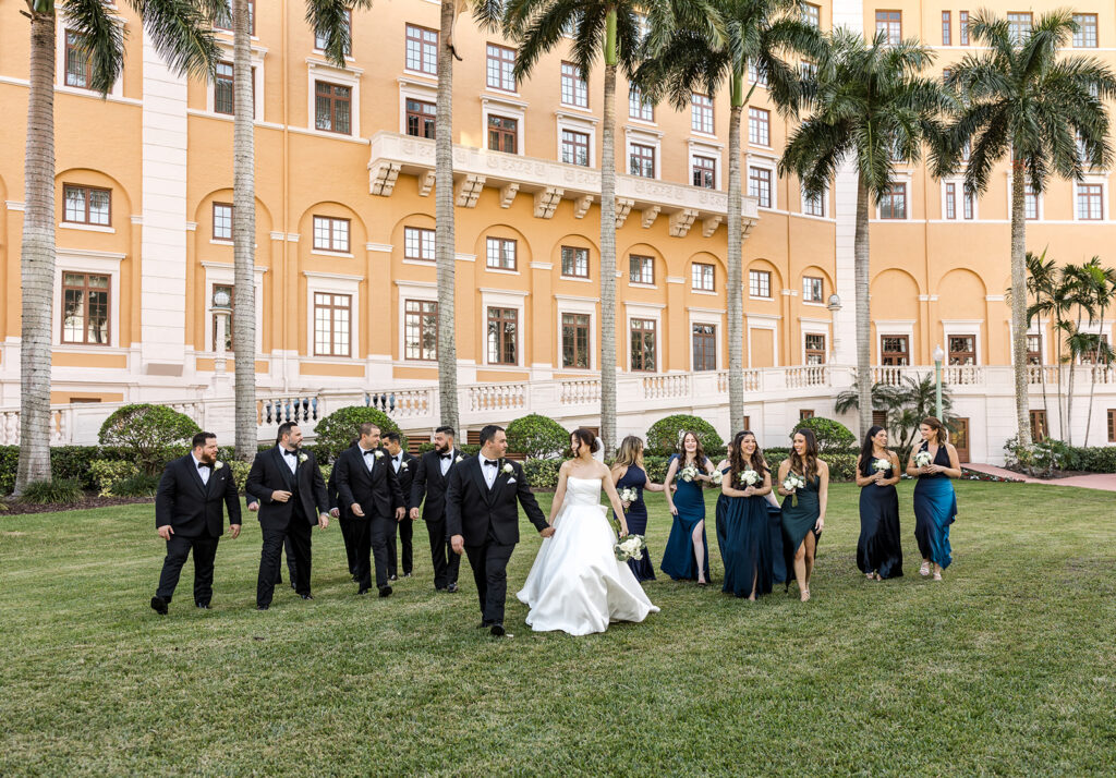 Full wedding party walking on the lawn in front of the iconic Biltmore facade for a Miami city weddings photo.