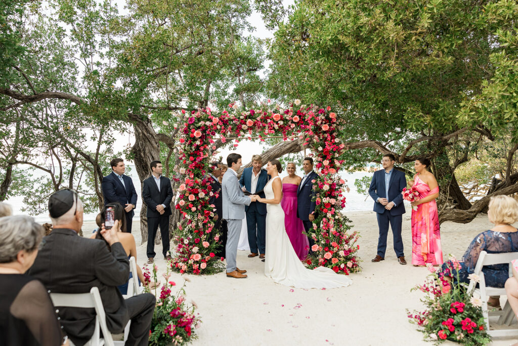 Tropical beach wedding ceremony under a dense red floral arch for Key Largo weddings.