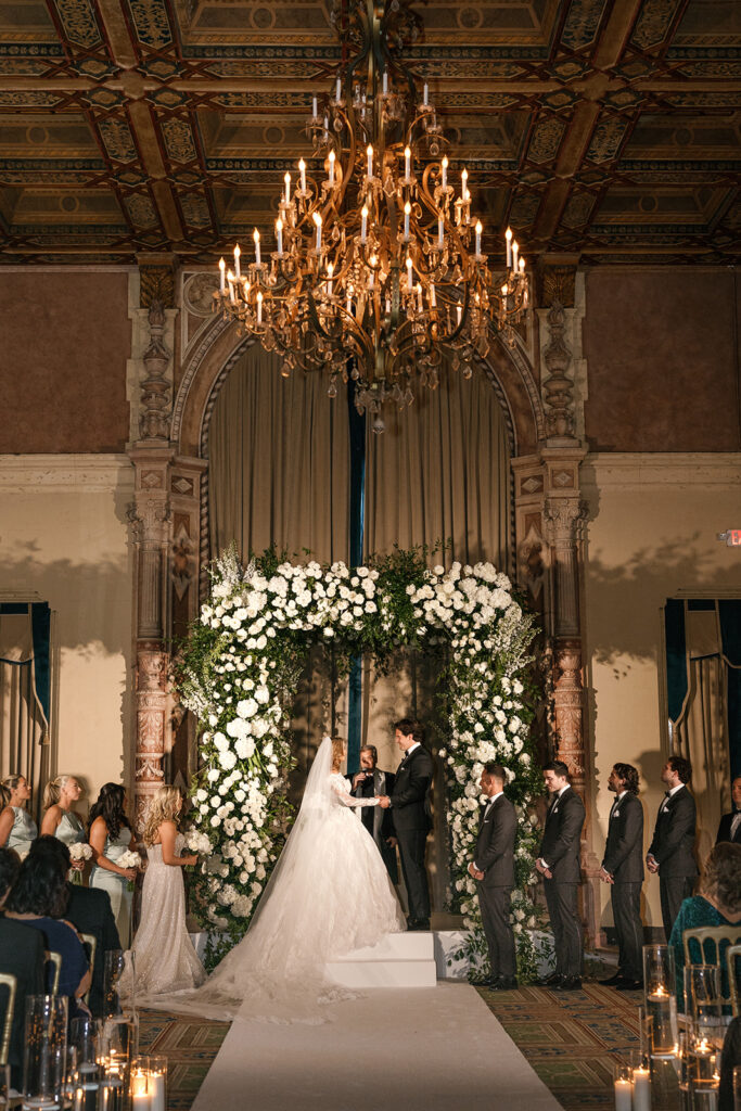 Opulent indoor ceremony under a floral arch at the historic Biltmore Hotel, a beautiful Miami weddings venue.