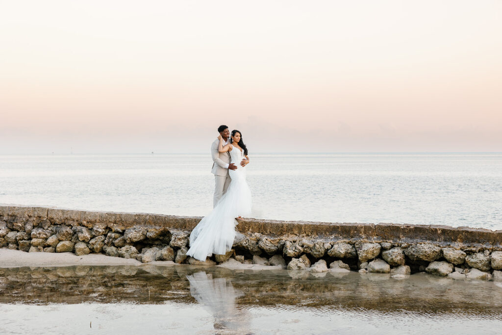 Bride and groom standing on a low jetty in the calm ocean water during their Florida Keys weddings portrait session.