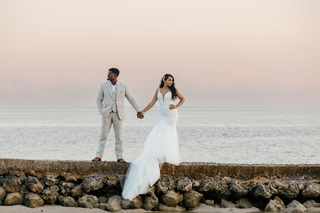 Bride and groom on a low stone jetty with water reflection at sunset for a Florida Keys wedding.